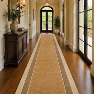 Puede incluir: Una alfombra larga y rectangular para pasillo con un centro marrón claro, bordeada por un marrón medio y crema. La alfombra está colocada sobre un suelo de madera oscura en un pasillo con puertas arqueadas y una puerta de madera oscura al final.