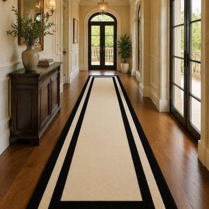 May include: A hallway with a cream-coloured runner rug with a black border. The runner is on a dark wood floor. The walls are painted a light beige, and there are arched windows and a dark wood door at the end of the hall.