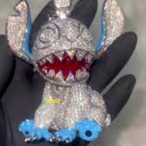 Puede incluir: Un colgante con incrustaciones de diamantes con forma de personaje de dibujos animados con orejas y pies azules y boca roja. El colgante se sostiene en una mano enguantada de negro. La palabra "antique" es visible.