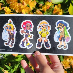 May include: A sticker sheet featuring four colorful cartoon characters with ink-like hair and outfits. The characters have various expressions and poses, set against a black background. The sticker sheet has the text "@deepseasecret".