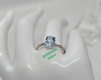 May include: A silver ring with a light blue oval gemstone. The ring has a twisted band and is set on a white background.