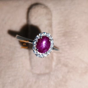 Op de afbeelding: Een zilveren ring met een rode robijn edelsteen omringd door een halo van kleinere diamanten.