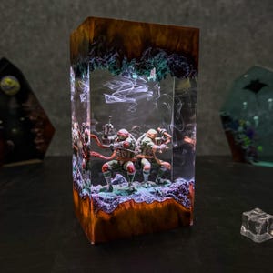 May include: A rectangular resin sculpture featuring two Teenage Mutant Ninja Turtles figures. The sculpture has a brown and orange base with a green and purple top, and the figures are in the center. The sculpture is lit from within.