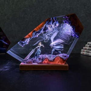 Może przedstawiać: Przezroczysta rzeźba z żywicy przedstawiająca scenę walki z dwiema postaciami, osadzona na drewnianej podstawie. Postacie są w dynamicznej pozie, z dużym mieczem. Żywica ma fakturę drewna i jest podświetlona fioletowym i białym światłem.