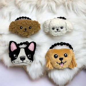 May include: Four plush dog-shaped hair accessories. The dogs are in various colors: brown, white, black and white, and tan. Each has a black elastic band with black beads. The black and white dog has pink ear accents.