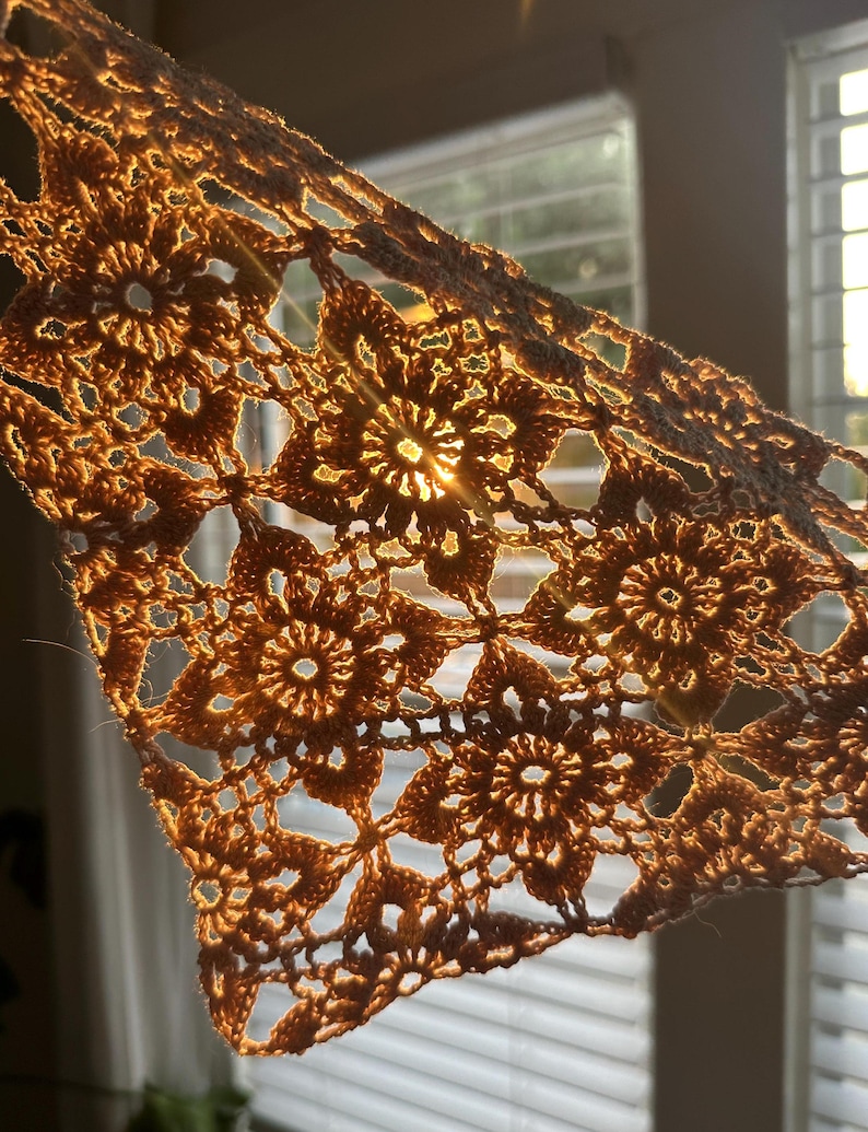 May include: A close-up of a crocheted lace doily with a sunbeam shining through it. The doily is a light brown color and has a delicate, intricate pattern.