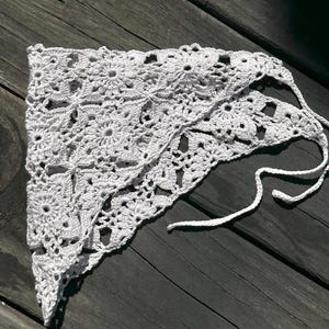 May include: White crocheted triangular scarf with a delicate floral pattern and tied ends.
