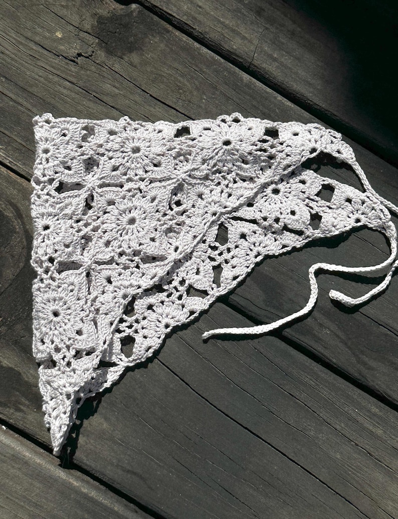 May include: White crocheted triangular scarf with a delicate floral pattern and tied ends.