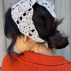 May include: A light gray crocheted headband with a square pattern. The headband is tied in a knot at the back of the head.
