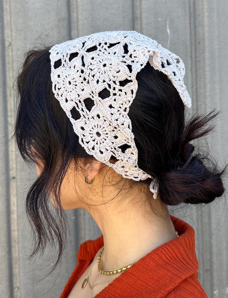 May include: A light gray crocheted bandana with a floral pattern. The bandana is tied around the head of a person with dark hair.