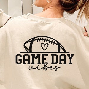 May include: A cream-colored sweatshirt with a black graphic of a football with a heart inside and the text "GAME DAY vibes".