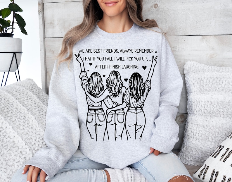 以下が含まれることがあります： グレーのトレーナーに、3人の女性が描かれた黒いグラフィックと「We are best friends. Always remember that if you fall I will pick you up... after I finish laughing.」というテキストがプリントされています
