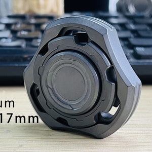 May include: A dark gray metal fidget spinner with a textured surface and a circular design. It measures 48x48x17mm and weighs 97g. Zirconium 48x48x17mm 97g