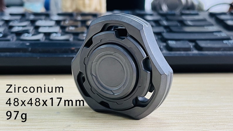 May include: A dark gray metal fidget spinner with a textured surface and a circular design. It measures 48x48x17mm and weighs 97g. Zirconium 48x48x17mm 97g