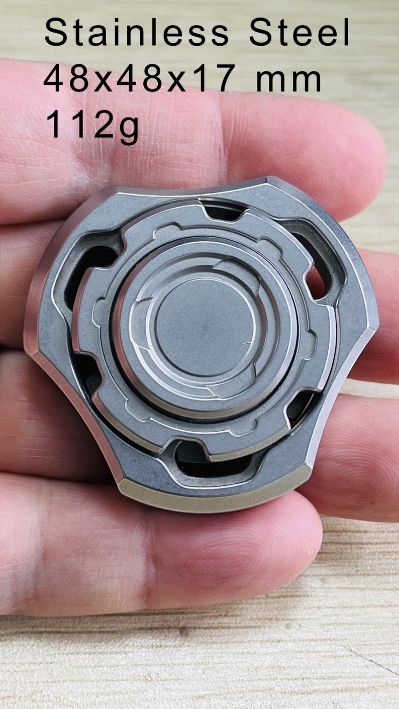 May include: A silver metal fidget spinner with a gear design. It measures 48x48x17 mm and weighs 112 grams.