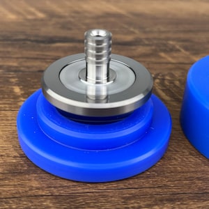 Op de afbeelding: Een zilveren metalen bovenkant met een blauwe siliconen basis. De bovenkant heeft een schroefdraadopening en een glad, afgerond oppervlak. De basis bestaat uit drie gestapelde ringen.