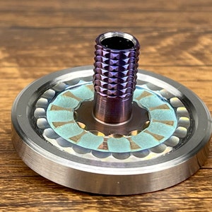 May include: A spinning top with a purple and silver finish. The top has a decorative design with a light blue and gold pattern.