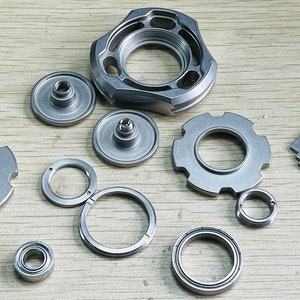 May include: A set of silver metal parts for a fidget spinner, including a central bearing, a top cap, a bottom cap, a ring, and a bearing spacer.