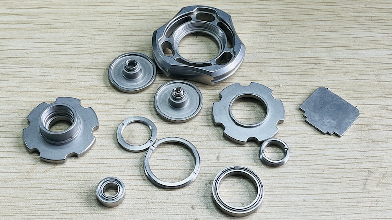 May include: A set of silver metal parts for a fidget spinner, including a central bearing, a top cap, a bottom cap, a ring, and a bearing spacer.