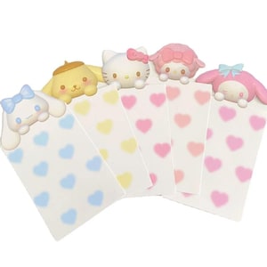 Pode incluir: Cinco cartões de notas coloridos com padrões de corações, cada um com um personagem diferente da marca Sanrio. Os personagens são Hello Kitty, My Melody, Little Twin Stars, Pompompurin e Cinnamoroll.