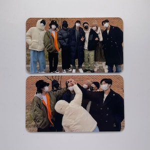May include: A group of people wearing face masks and winter clothing stand in front of a brick wall. Some are wearing hats and some are wearing coats.
