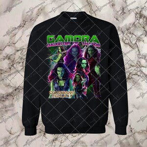 May include: Black sweatshirt with a green, purple, and red graphic print of Gamora from Guardians of the Galaxy. The text "Gamora Daughter of Thanos" is printed in white on the shirt.