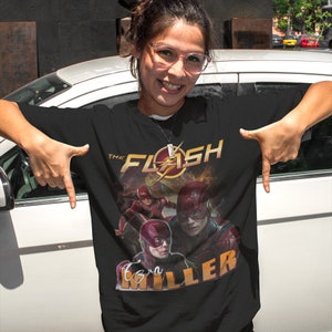 Może przedstawiać: Czarny T-shirt z grafiką przedstawiającą Flasha, z wizerunkiem Ezry Millera. Grafika zawiera tekst "The Flash" i "Ezra Miller".