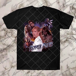 May include: Black t-shirt with a graphic print of Pepper Potts from the Marvel Cinematic Universe. The graphic features Pepper Potts, Iron Man, Rescue, and other characters from the Iron Man movies. The text "Pepper Potts" is printed in white letters on the graphic.