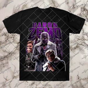Op de afbeelding: Een zwart T-shirt met een paarse afbeelding van Baron Zemo uit het Marvel Cinematic Universe. De afbeelding toont Zemo met een paars masker en een bontjas. De tekst "BARON ZEMO" staat in grote paarse letters boven de afbeelding.