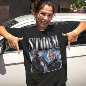 May include: Black t-shirt featuring a graphic of Storm from the X-Men comics. The graphic is in a retro style with the word "STORM" in large, silver letters above the image.