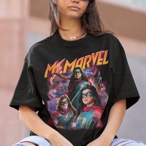 May include: Black t-shirt featuring a graphic print of Ms. Marvel characters in a comic book style. The text "Ms. Marvel" is printed in yellow and orange lettering.
