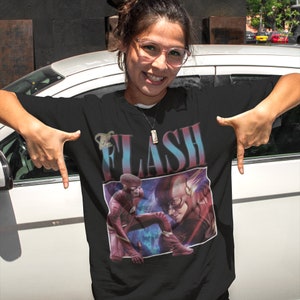 May include: Black t-shirt with a vintage-style graphic of The Flash, featuring a red and yellow lightning bolt design. The text "The Flash" is printed in a bold, colorful font.