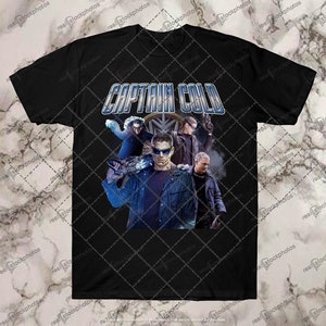 May include: Black t-shirt with a graphic of Captain Cold from the DC Comics universe. The graphic features Captain Cold and his team, including his brother, Mirror Master, and his partner, Heat Wave. The graphic is in a retro style with a blue and white color scheme.