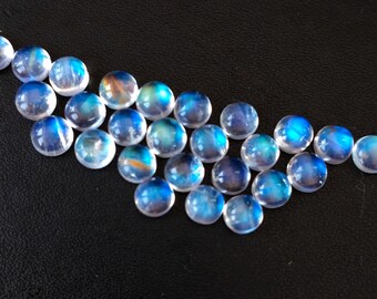 Puede incluir: Una colección de cabujones de piedra lunar iridiscente en varios tonos de azul y blanco. Las piedras son redondas y lisas, con un brillo sutil.