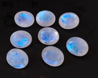 May include: Eight oval-shaped moonstone gemstones with a white iridescent sheen and blue flashes.