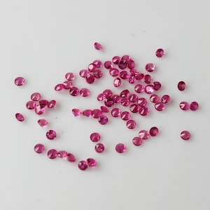 Może przedstawiać: Rozproszenie małych, okrągłych, różowych kamieni szlachetnych na białym tle.
