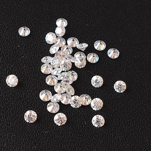 May include: A collection of small, clear, round, faceted gemstones, scattered on a black surface.