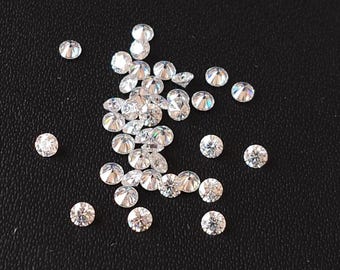 May include: A collection of small, clear, round, faceted gemstones, scattered on a black surface.
