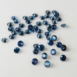 Op de afbeelding: Een verzameling ronde, gefacetteerde, blauwe edelstenen. De edelstenen zijn verspreid over een wit oppervlak.