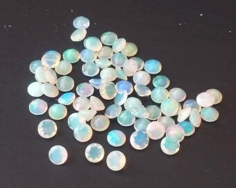 May include: A collection of iridescent opal gemstones, displaying a range of colors including white, blue, and green. The opals are round and oval-shaped, with a polished, faceted surface. The gemstones are scattered on a dark surface.