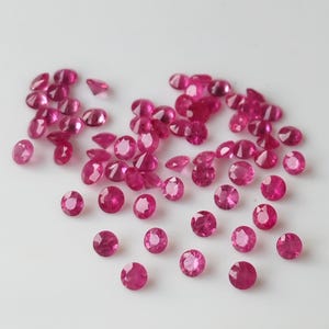 Może przedstawiać: Kolekcja okrągłych, różowych kamieni szlachetnych, prawdopodobnie rubinów, rozrzuconych na białym tle. Kamienie szlachetne są fasetowane i mają błyszczące, błyszczące wykończenie.