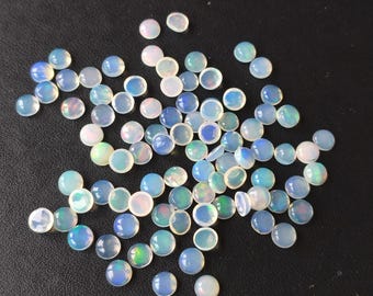 May include: A collection of small, round, translucent cabochons with an opalescent finish. Each piece displays a milky white base with subtle flashes of blue, green, and pink iridescence when light hits the smooth, domed surface of these loose gemstones.
