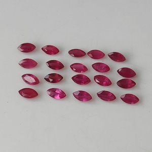 Puede incluir: Una colección de gemas rojas oscuras de forma ovalada. Las gemas están dispuestas en filas, mostrando sus superficies pulidas y su color vibrante. Estas gemas son probablemente rubíes, ideales para joyería.