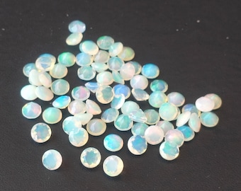 Può includere: Una collezione di opali rotondi e sfaccettati, con una base bianco latte e lampi iridescenti di blu, verde e rosa. Le pietre preziose sono sparse su una superficie scura, mostrando le loro superfici lucide e le variazioni naturali.