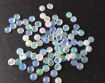 May include: A collection of small, round, translucent cabochons with an opalescent finish. Each piece displays a milky white base with subtle flashes of blue, green, and pink iridescence when light hits the smooth, domed surface of these loose gemstones.