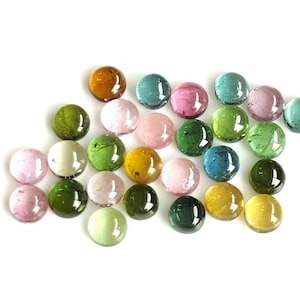May include: Assortment of round, smooth, colourful gemstones in various shades of green, pink, brown, and blue. The gemstones are arranged in a loose cluster on a white background.