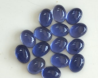 May include: A collection of oval-shaped, polished gemstones in varying shades of blue. The gemstones are arranged on a white surface, each reflecting light and exhibiting a smooth, glossy texture. The overall composition suggests a focus on jewelry or crafting materials.