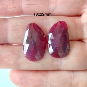 May include: Two faceted ruby gemstone drops, each measuring 13x22mm. The stones are a deep red color and have a faceted cut.