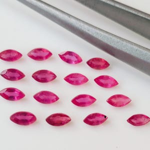 Puede incluir: Una colección de 16 piedras preciosas de rubí de forma marquesa, dispuestas en filas sobre una superficie blanca. Los rubíes son de color rosa intenso y tienen un alto nivel de brillo.
