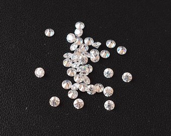 May include: A scattering of small, clear, round, faceted gemstones on a black surface.